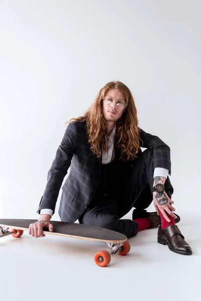 Stylischer Geschäftsmann mit lockigem Haar sitzt mit Longboard auf dem Boden — Stockfoto