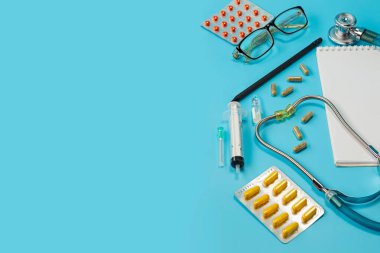 Gözlüklü steteskop, not defteri ve kalem, ilaç ve termometre, mavi doktor masasında ya da metin için fotokopi masası olan hemşire masasında. Sağlık kontrolü. Sağlık ve tıp geçmişi var. Hasta teşhisi için doktor gereci. Kardiyoloji doktoru.