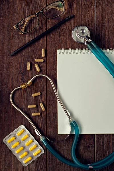 Health medical concept. A stethoscope, notepad, glasses and pills on a wooden background. Medical healthcare and medicine background.