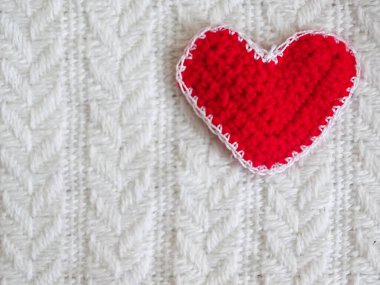 Yumuşak örülmüş kırmızı kalp beyaz örülmüş battaniye üzerinde yatıyor..
