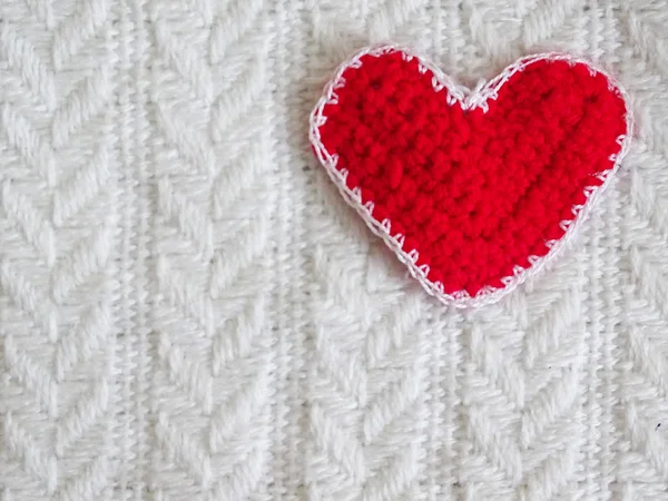 Soft knitted red heart lying on white knitted blanket plaid.