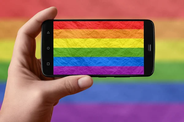 LGBT flag on the phone screen. Smartphone in hand photographing flag.