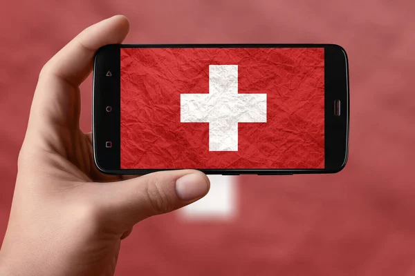 Switzerland flag on the phone screen. Smartphone in hand photographing flag.