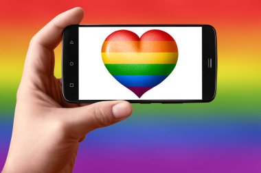 Telefon ekranında kalp şeklinde bir Lgbt bayrağı var. Eldeki akıllı telefon bir kalp bayrağı gösteriyor. 