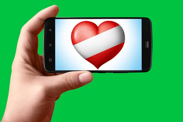 오스트리아는 전화 화면에서 심장 모양으로 깃발을 그린다. 손에 들고 있는 스마트폰에는 크로마의 주요 배경 화면에 플래그 하트가 보 입니다.. — 스톡 사진
