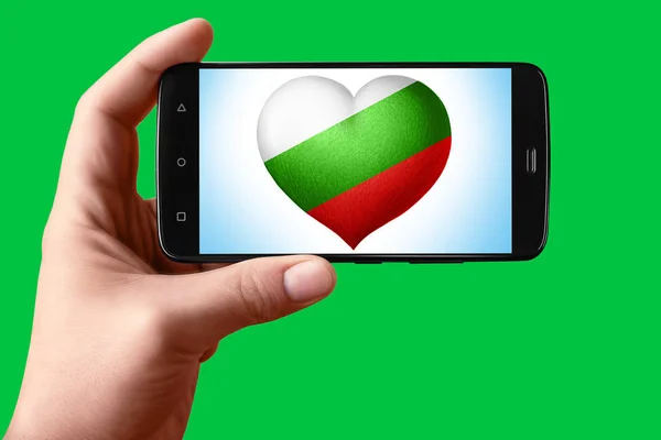 불가리아는 전화 화면에서 심장 모양으로 깃발을 그린다. 손에 들고 있는 스마트폰에는 크로마의 주요 배경 화면에 플래그 하트가 보 입니다.. — 스톡 사진