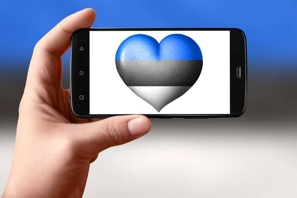 에 스토니아는 전화 화면에서 심장 모양으로 깃발을 그린다. 손에 들고 있는 스마트폰에 하트 플래그가 보 입니다.. — 스톡 사진