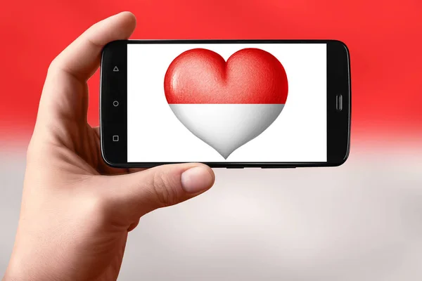 Monaco flagga i form av ett hjärta på telefonskärmen. Smartphone i handen visar ett hjärta flagga. — Stockfoto