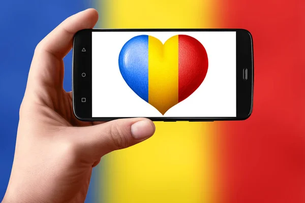 루마니아는 전화 화면에서 심장 모양으로 깃발을 그린다. 손에 들고 있는 스마트폰에 하트 플래그가 보 입니다.. — 스톡 사진
