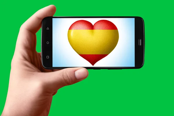 스페인은 전화 화면에서 심장 모양으로 깃발을 그린다. 손에 들고 있는 스마트폰에는 국기의 심장 이 배경에 있는흐 로마 키 (hromakey) 가 보인다. — 스톡 사진