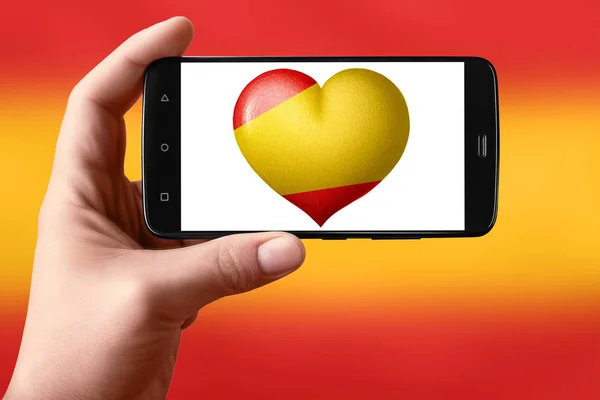 스페인은 스크린에 심장 모양으로 깃발을 그린다. 손에 들고 있는 스마트폰에는 깃발 심장이 보인다. — 스톡 사진