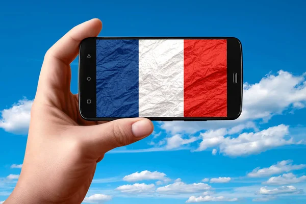 Flaga Francji na ekranie telefonu. Smartfon w ręku pokazuje flagę na tle nieba z chmurami. — Zdjęcie stockowe