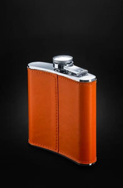 Flask for alcohol. Steel flaa with orange leather trim stands on a black background. Capacity for whiskey, rum, vodka and various alcohol.