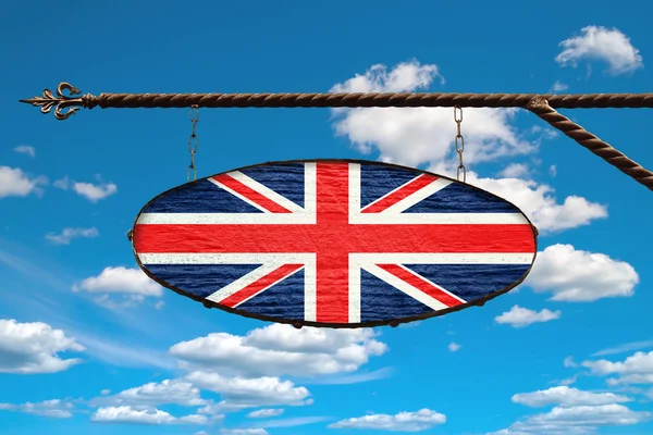 Britain flag on an old signboard. An oval sign in the colors of the flag of Britain hangs on a metal forged structure. Template on a background of blue sky with clouds.