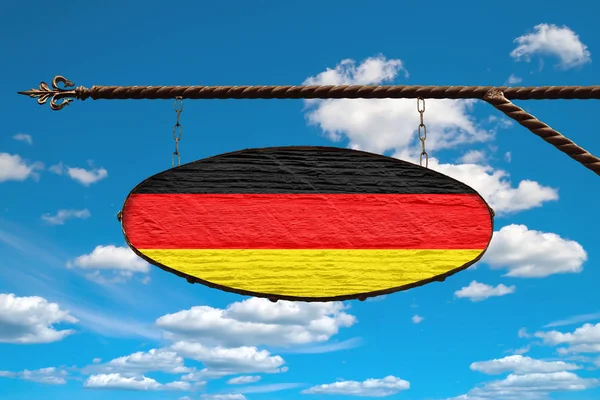 Germany flag on signboard. Oval sign in the colors of the flag of Germany hanging on a metal forged design. Template on a background of blue sky with clouds. — Stockfoto