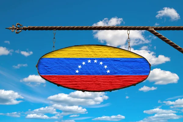 Venezuela flag on a signboard. Oval signboard colors flag Venezuela hangs on a metal forged structure. Template on a background of blue sky with clouds.