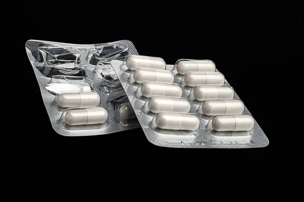Medicina. Pillole di capsula bianca in un blister intero e aperto su uno sfondo nero. Concetto sanitario. Antibiotici e compresse di capsule antimicrobiche. Industria farmaceutica . — Foto Stock