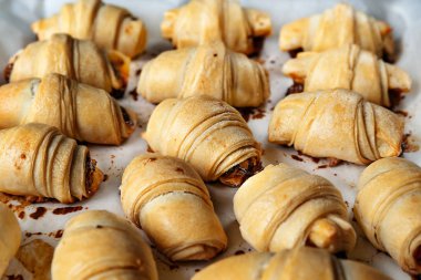 Homemade baking. A lot of fresh sweet spring rolls are piled on parchment paper, on a baking sheet.