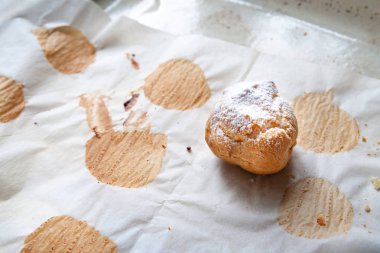 Homemade baking. A freshly baked hot sweet burger sprinkled with icing sugar lies on baking paper on an empty baking sheet.