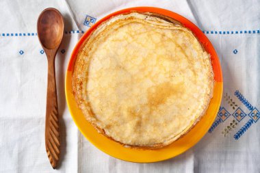 Bir yığın krep. Tabakta ince krepler ve tahta bir kaşık. Geleneksel köy yemekleri. Halk mutfağı..