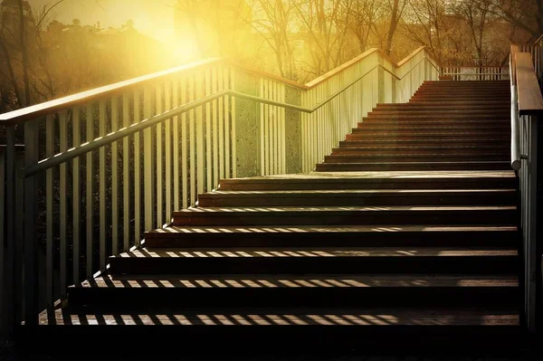 Staircase with a shadow. Sunlight on a staircase with wooden steps and metal railing. A play of light and shadow in the evening. Conceptual image.