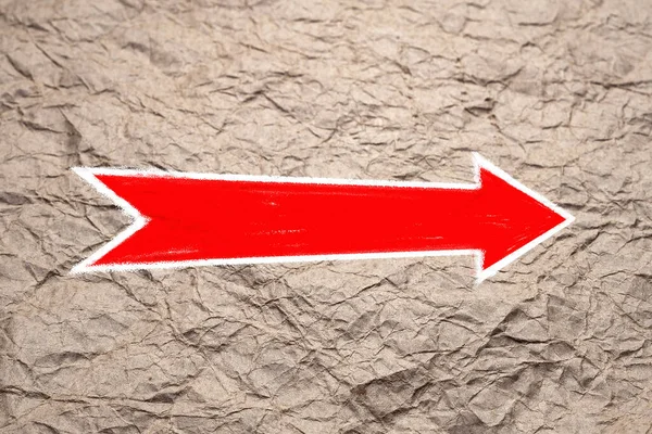 Arrow on the textured surface. Red arrow pointer is drawn on crumpled craft paper. Direction indicator. Signs and pointers.