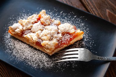 Ev yapımı kayısılı turta. Siyah bir tabakta pudra şekerli ve çatallı bir parça sade sıcak kek. Doğal organik gıda. Seçici yumuşak odaklanma. Ev mutfağı.