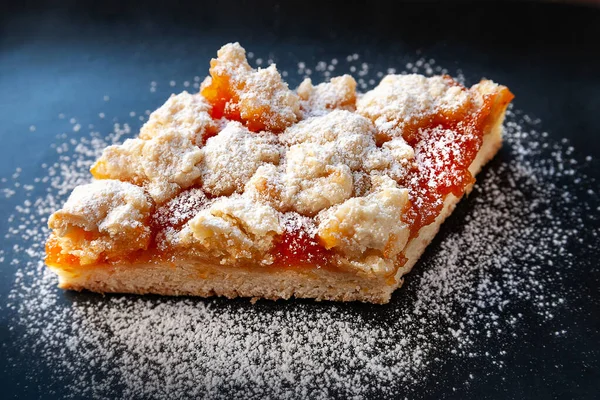 Homemade apricot pie. A slice of rustic hot sweet pie in icing sugar on a black plate. Natural organic food. Selective soft focus. Home kitchen.