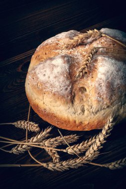Ev yapımı ekmek. Tahta arka planda bir somun taze köylü ekmeği ve buğday dikenlerinin yakın çekimi. Ev yapımı pişirme. Tonu ayarlanmış resim.