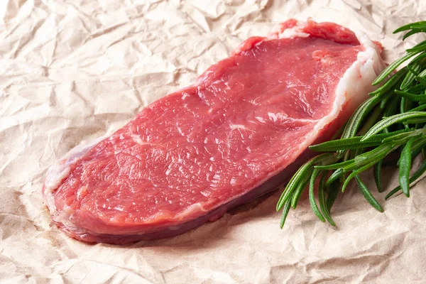 Raw meat. Closeup slice of fresh juicy raw meat and a rosemary branch on paper. Preparing meat for a barbecue. Healthy, natural food.