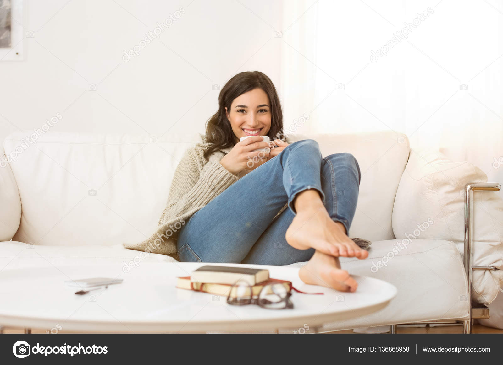 Garota feliz com telefone relaxa no sofá ou no sofá da sala