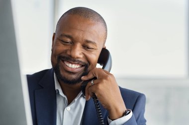 Olgun siyahi iş adamı telefonda konuşuyor.