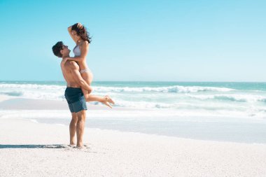 Sevgi dolu çift sahilde fotokopi odasıyla sarılıyor. Eş kılıklı mutlu sevgili, arka planda okyanusla gülümseyen kız arkadaşını kaldırıyor. Yakışıklı koca güzel karısını bikinisiyle kumsalda eğlenirken taşıyor..