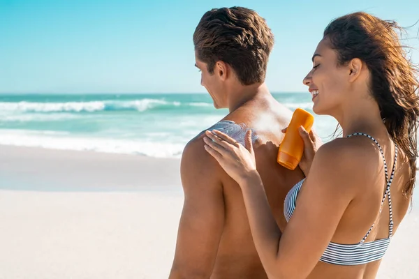 해변에서 친구에게 로션을 바르는 해변에서 일광욕으로 남자한테 자외선 차단제를 바르는 — 스톡 사진