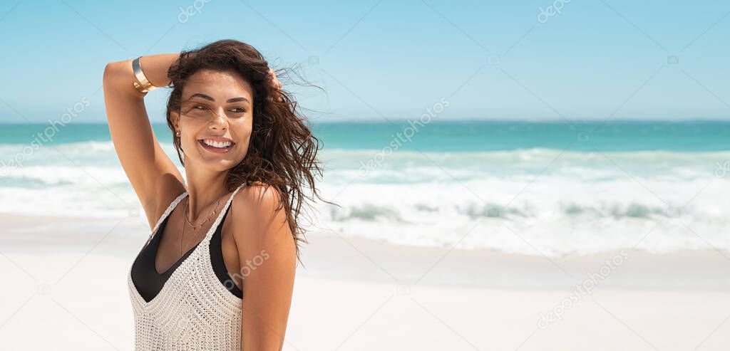 Latin stylish woman relaxing at tropical beach during summer vacation. Portrait of carefree tanned girl relaxing at sea with copy space. Young smiling woman enjoying breeze in a sunny day while looking away.