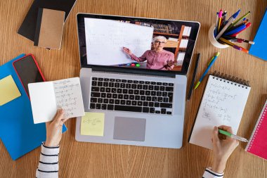 Evde dizüstü bilgisayarlı öğretmenle yüksek açılı video konferansı. Üniversite öğrencisi internetten webinar izlerken, ses kurslarını dinlerken matematik öğreniyor. Bilgisayar, mesafe ve e-öğrenim eğitimi hocasıyla videodaki en iyi kız görüntüsü.