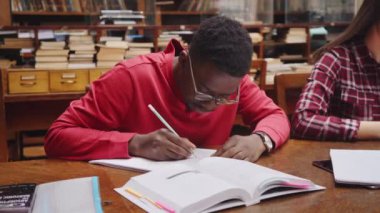Üniversite öğrencisi kütüphanede ders çalışırken gözlük takıyor. Genç Afrikalı adam kütüphanede otururken kitaptan notlar alıyor. Ev ödevi sırasında notlar yazan sıradan bir adam..
