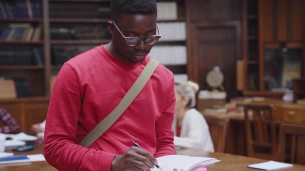 Estudante Negro Feliz Vestindo Óculos Lendo Livro Biblioteca Enquanto Olha — Vídeo de Stock