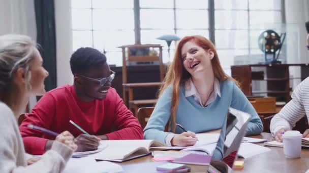 幸せな大学生が一緒に勉強して笑っています 大学図書館に座っている間に本を笑って勉強している多民族の友人のグループ 一緒に勉強する高校生の男女 — ストック動画