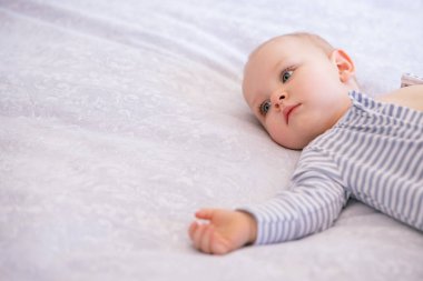 Altı aylık bir bebeğin portresi, fotokopi aletiyle yatakta yatıyor. Tatlı küçük çocuk başka tarafa bakıyor. Sevimli çocuk beyaz ve açık mavi çizgili bir beden giyiyor..