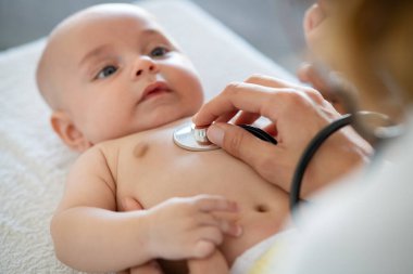 Doktor, klinikte steteskoplu küçük bir çocuğu muayene ediyor. Doktor steteskoplu küçük çocukların ciğerlerini dinliyor. Kalp atışlarını dinlemek ve kontrol etmek için steteskop kullanarak çocuk doktorunun elini kapat..