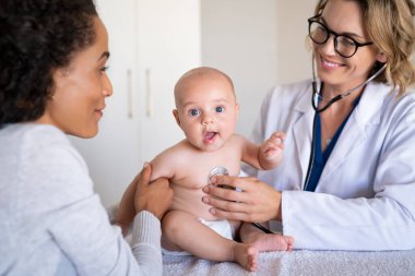 Bayan gülümseyen doktor klinikte steteskopla bebeğini muayene ediyor. Annesiyle birlikte doktor tarafından kontrol edilen şirin bir çocuğun portresi. Çocuk doktoru steteskopla bebeğini muayene ediyor.. 