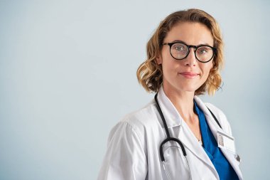 Kameraya bakan mutlu orta yaşlı doktor portresi. Mutlu, olgun bir çocuk doktoru mavi arka planda fotokopi çekerek duruyor. Steteskop ve işçi ceketi olan güvenilir pratisyen kadın..