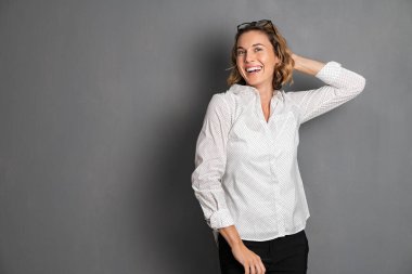 Gri arka planda gülümseyen ve kameraya bakan heyecanlı orta yaşlı kadın portresi. Neşeli genç iş kadını işten sonra resmi olarak dinleniyor. Güzel Alman kızı kameraya poz veriyor ve dans ediyor. Büyük bir sırıtışla ve kopyalayarak..