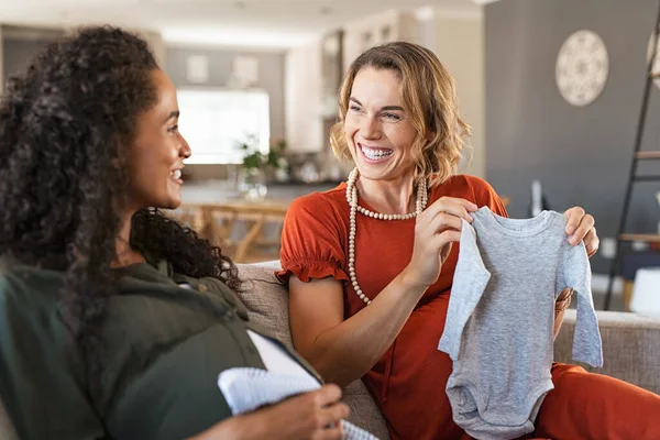 Donna Incinta Felice Guardando Vestiti Del Bambino Con Gioioso Amico — Foto Stock