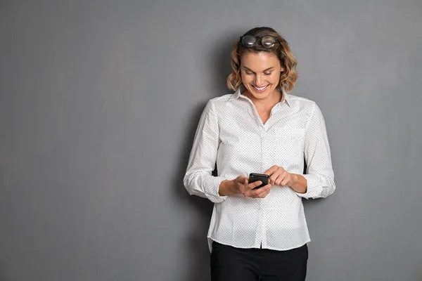 Vrolijke Zakenvrouw Staat Tegen Grijze Achtergrond Met Behulp Van Smartphone — Stockfoto