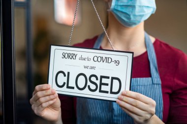 İş kadını, kapalı devre 19 nedeniyle iş faaliyetlerini kapatıyor. Cerrahi maskeli sahibi karantina koronavirüs hasarı nedeniyle dükkanının kapısını kapatmış. COVID-19 salgınının etkisiyle iflasın eşiğinde..