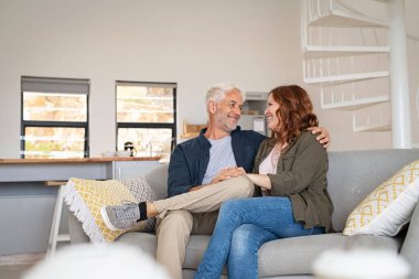 Emekli olgun çift kanepede birlikte oturuyor. Gülümseyen karısı olan yaşlı koca kanepede oturuyor ve birbirlerine bakarken kucaklaşıyorlar. Mutlu yaşlı çift el ele tutuşuyor..