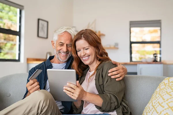 一对快乐的成熟夫妇坐在沙发上 在家里的数码平板电脑上网上购物 年长的丈夫和微笑的妻子在网上付账单 快乐的中年夫妇在网上支付数字平板电脑 复制空间 — 图库照片