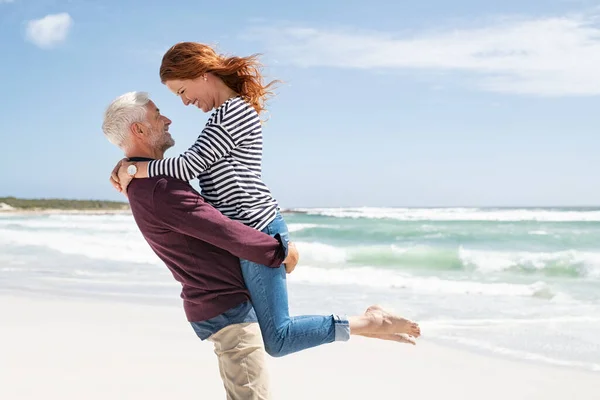 Зрелая Пара Обнимается Пляже Солнечный День Старший Активный Мужчина Поднимает — стоковое фото